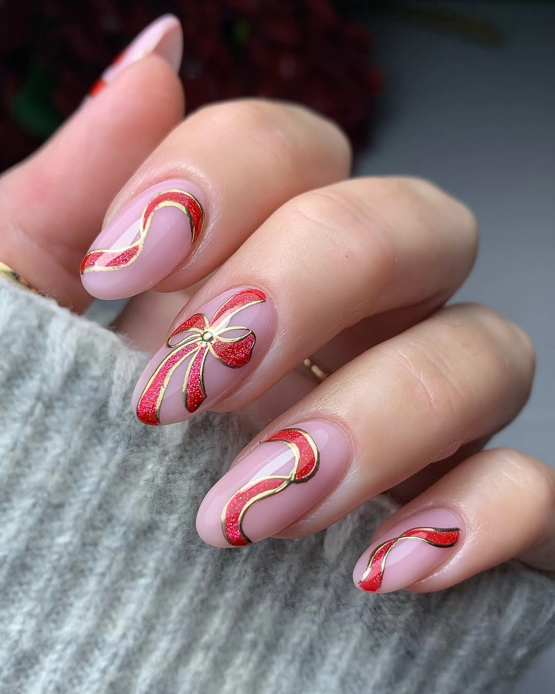 Long pink almond nails with curved red glitter ribbons and gold outlines.
