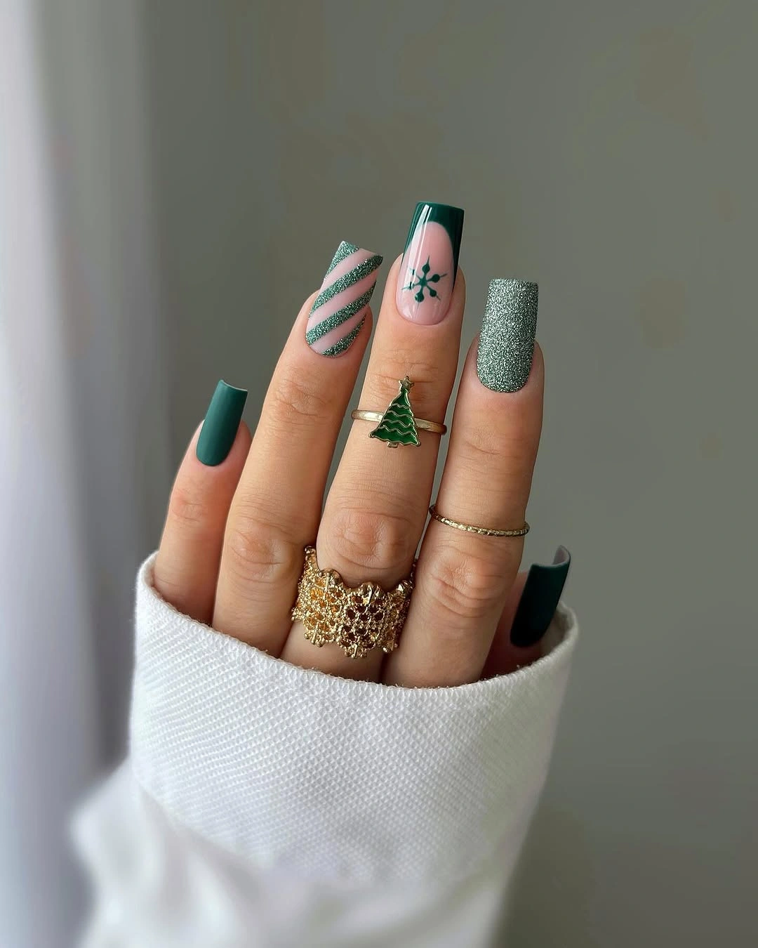 Long square nails with forest green polish, glitter, diagonal stripes, and starburst art.