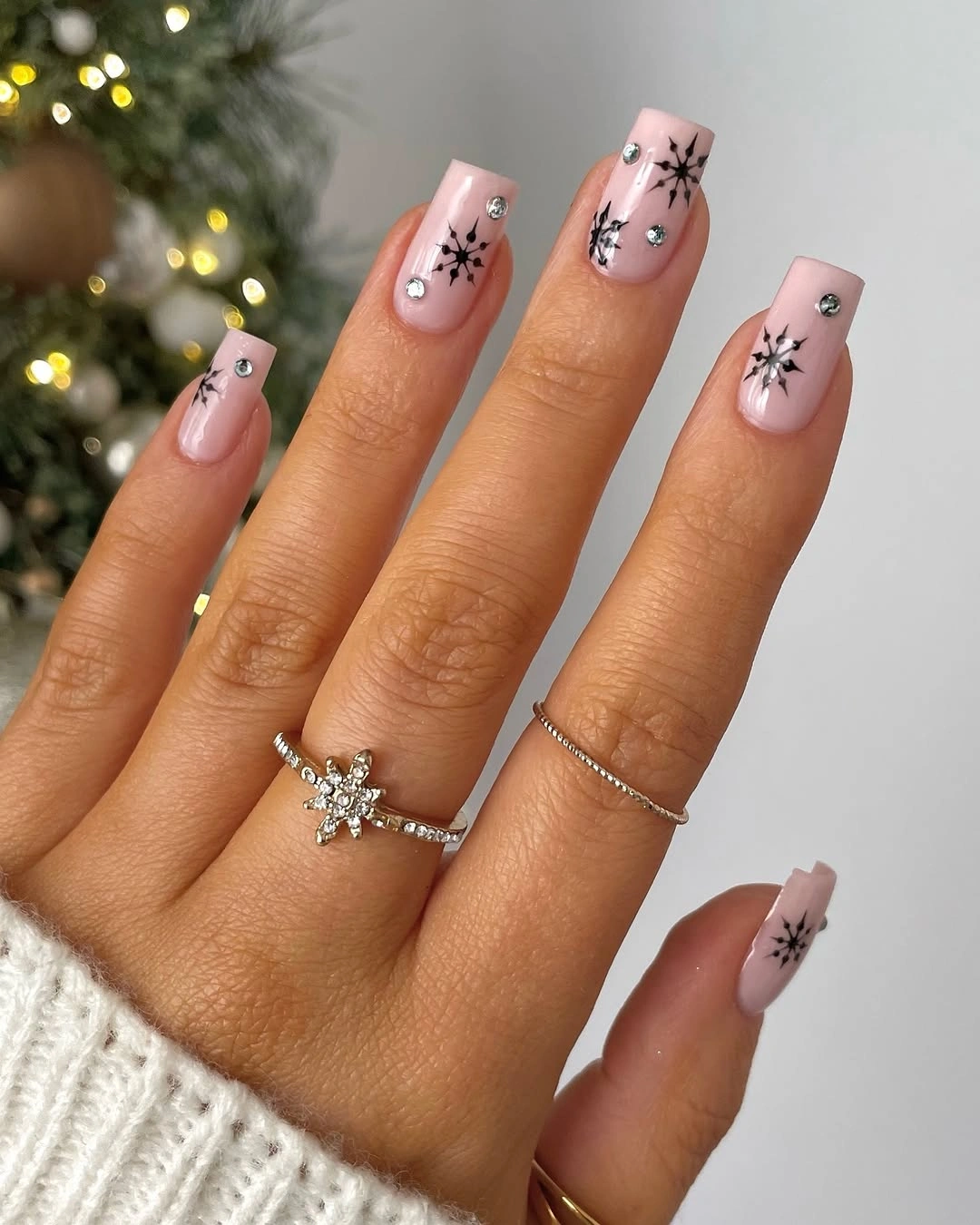 Light pink square nails with black snowflake motifs and reflective silver accents.
