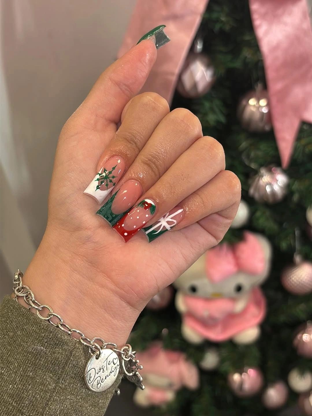 Long nude square nails with green tips, red accents, and white holiday patterns.