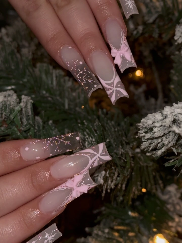 Long nude square nails with pink bows, white ribbons, and glitter accents.