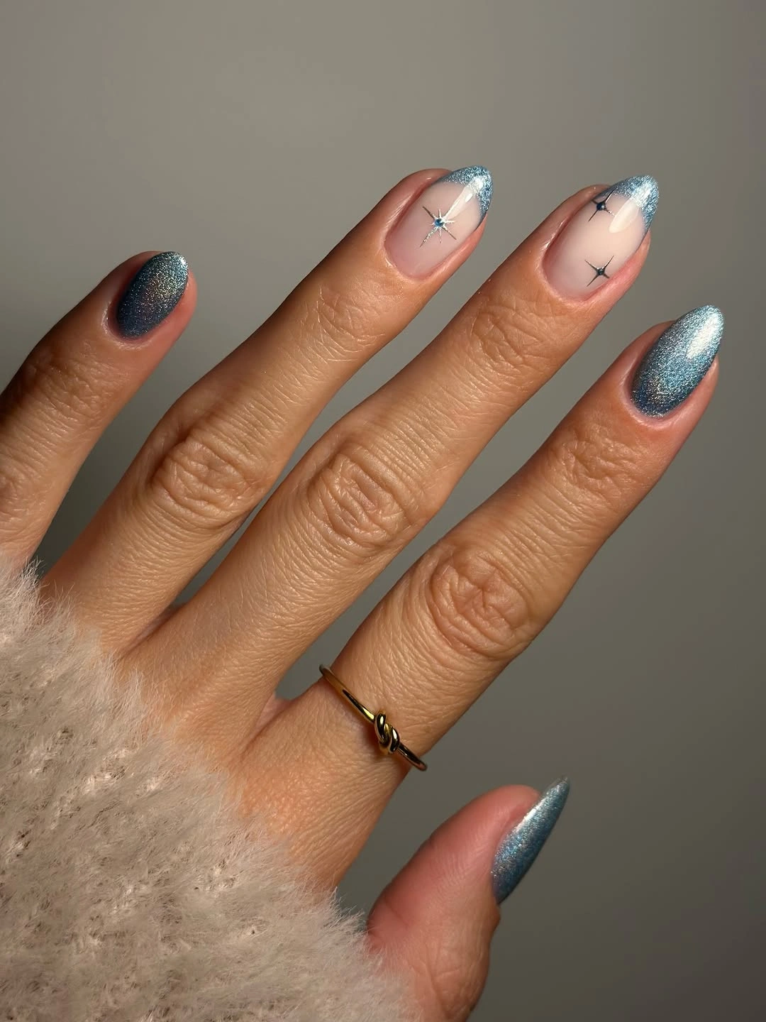 Almond nails with teal blue shimmer, metallic tips, and dark starburst accents.