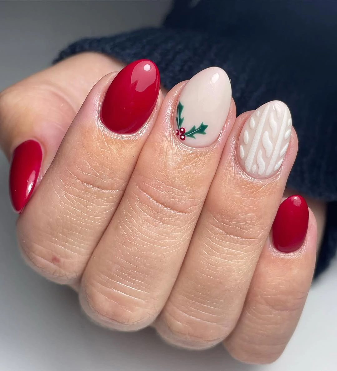 Rounded red and cream nails with green leaves and raised white knit patterns.
