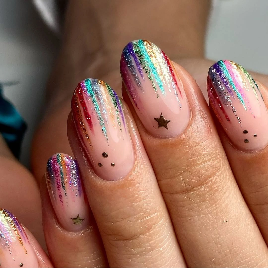Nude pink almond nails with multicolor glitter streaks, small stars, and dark dots.