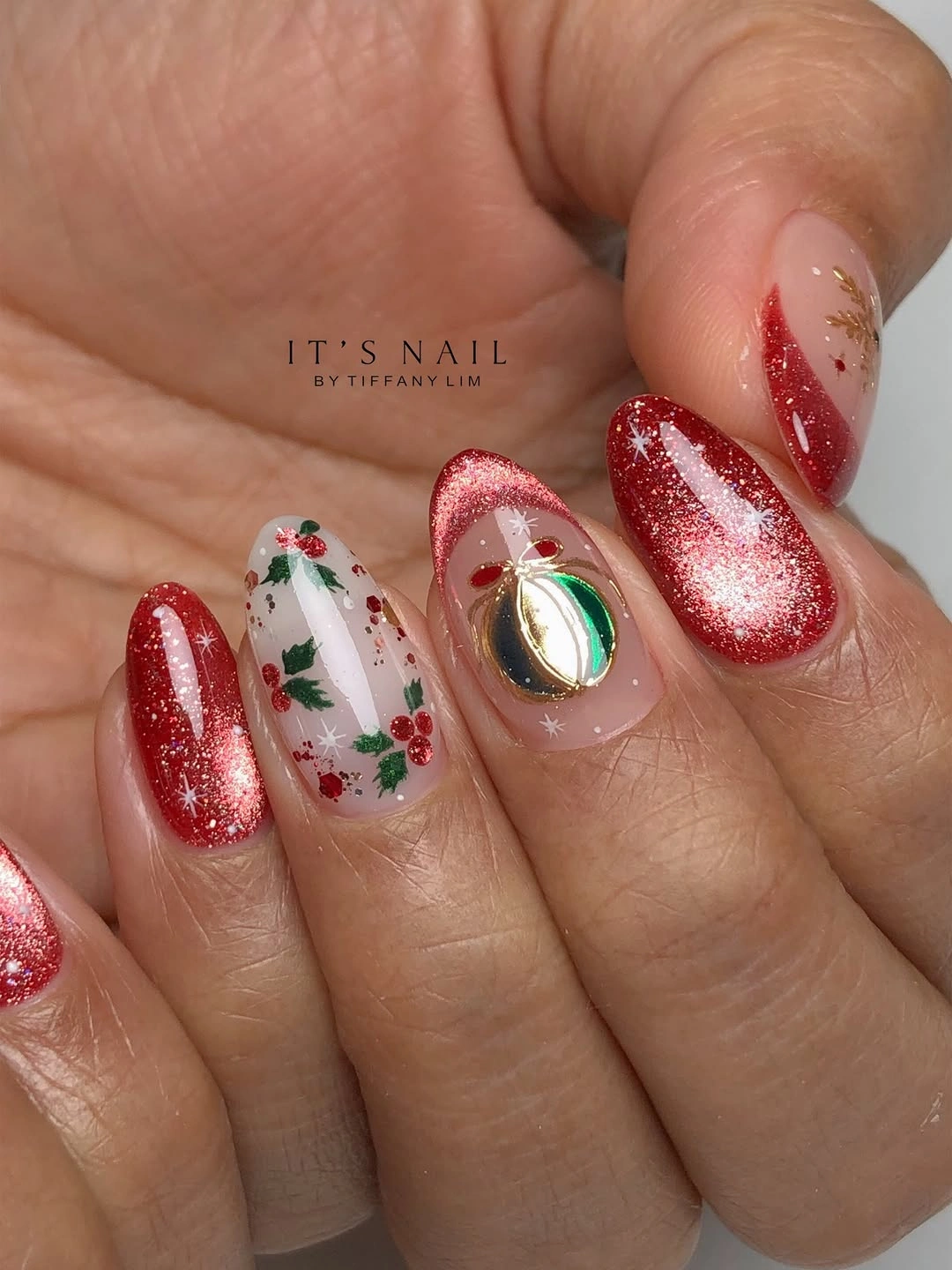 Red glitter nails with white snowflakes, green leafy motifs, and gold ornament accents.