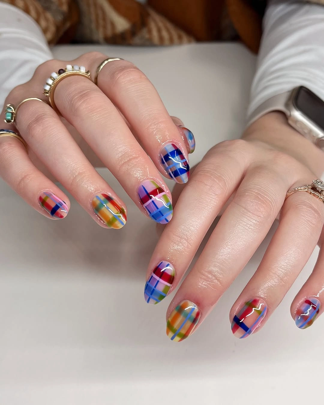 Rounded nails with blue, green, red, yellow, and orange plaid patterns.