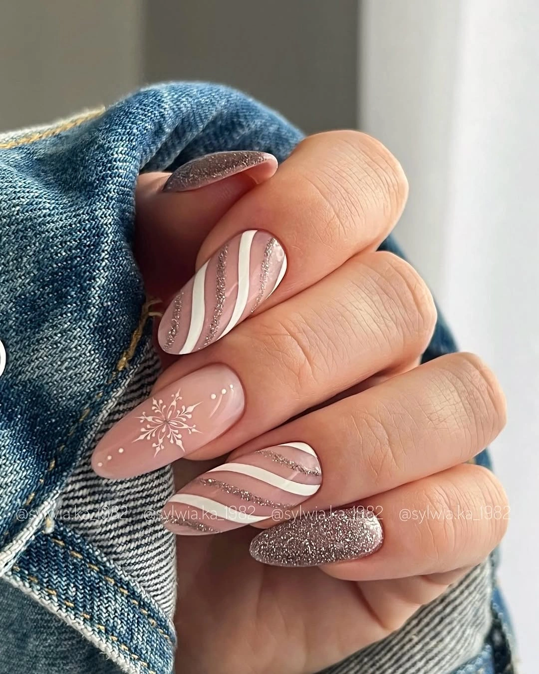 Nude taupe almond nails with white stripes, glitter accents, and snowflake art.
