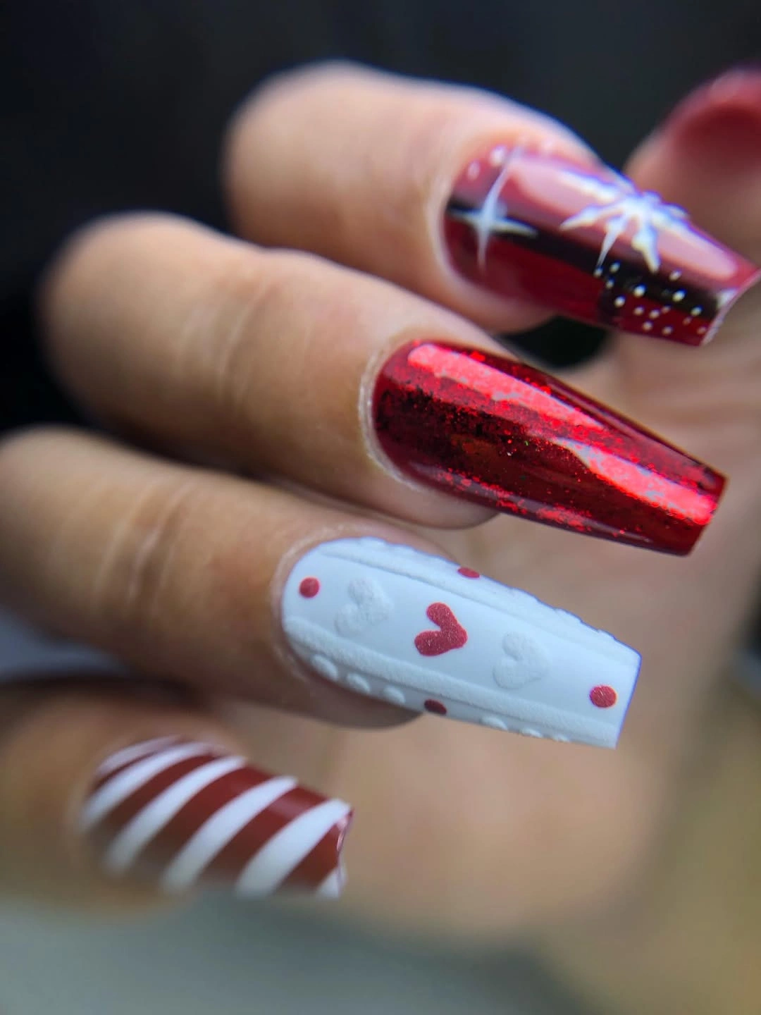 Long red glitter coffin nails with white starbursts and a textured-looking accent.