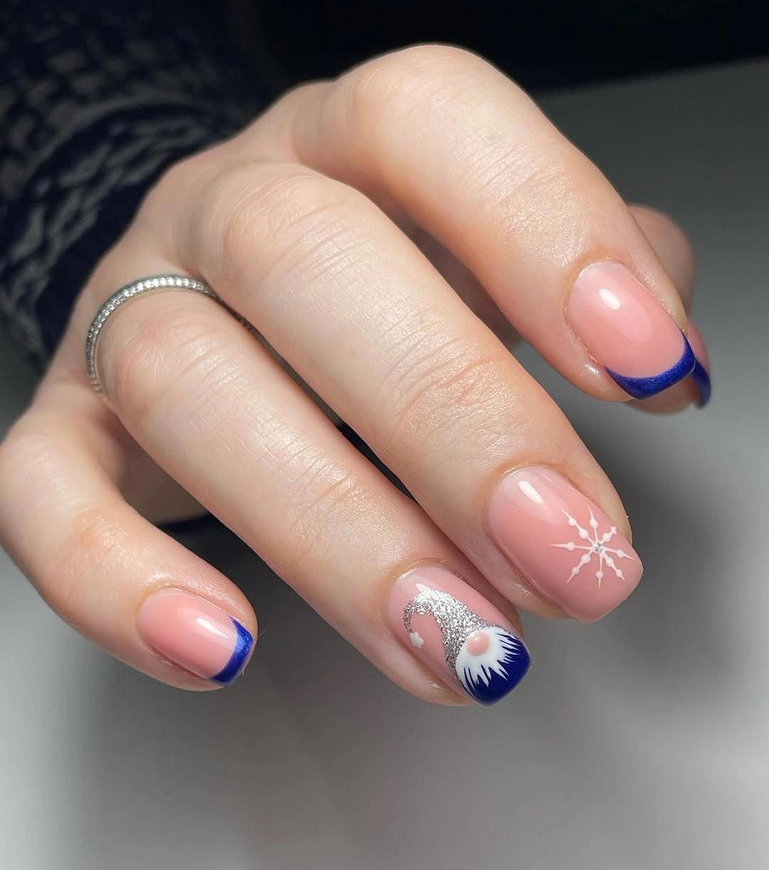 Pink nude nails with cobalt blue French tips and white snowflake accents.