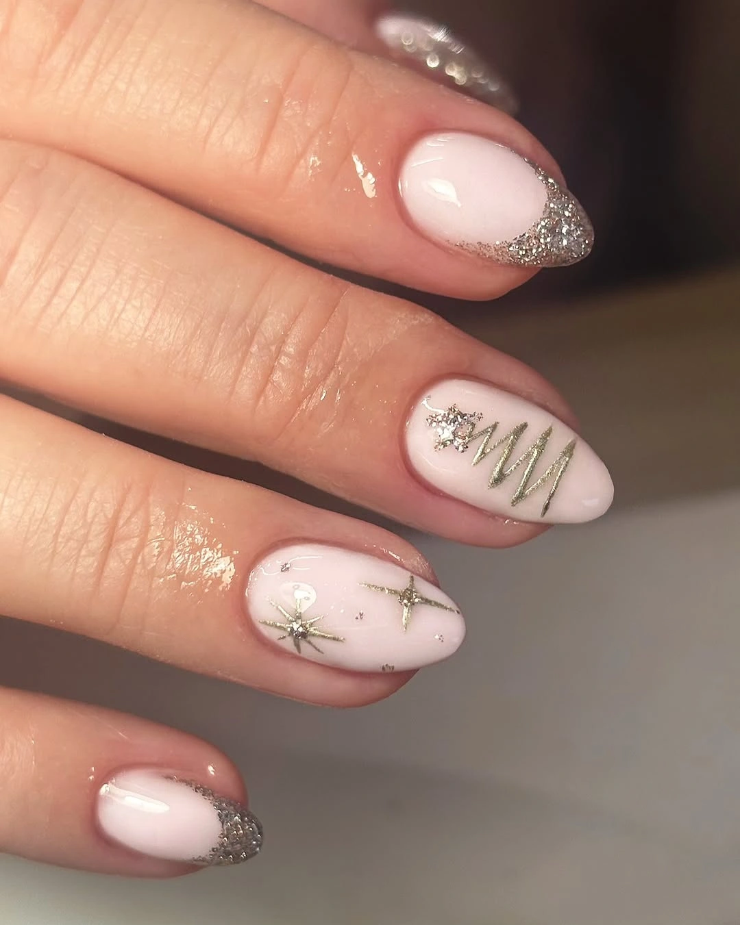 Pale pink almond nails with silver glitter tips and gold zigzag accents.