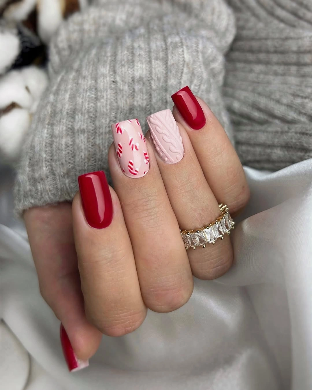 Glossy red square nails with candy cane prints and pale pink knit-like texture.
