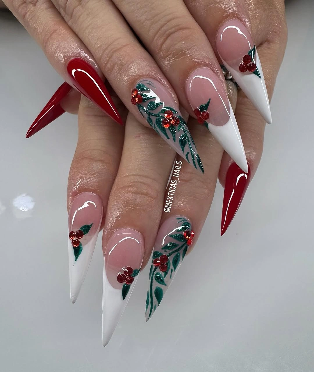Long stiletto nails with red polish, white tips, and greenery-like accents.