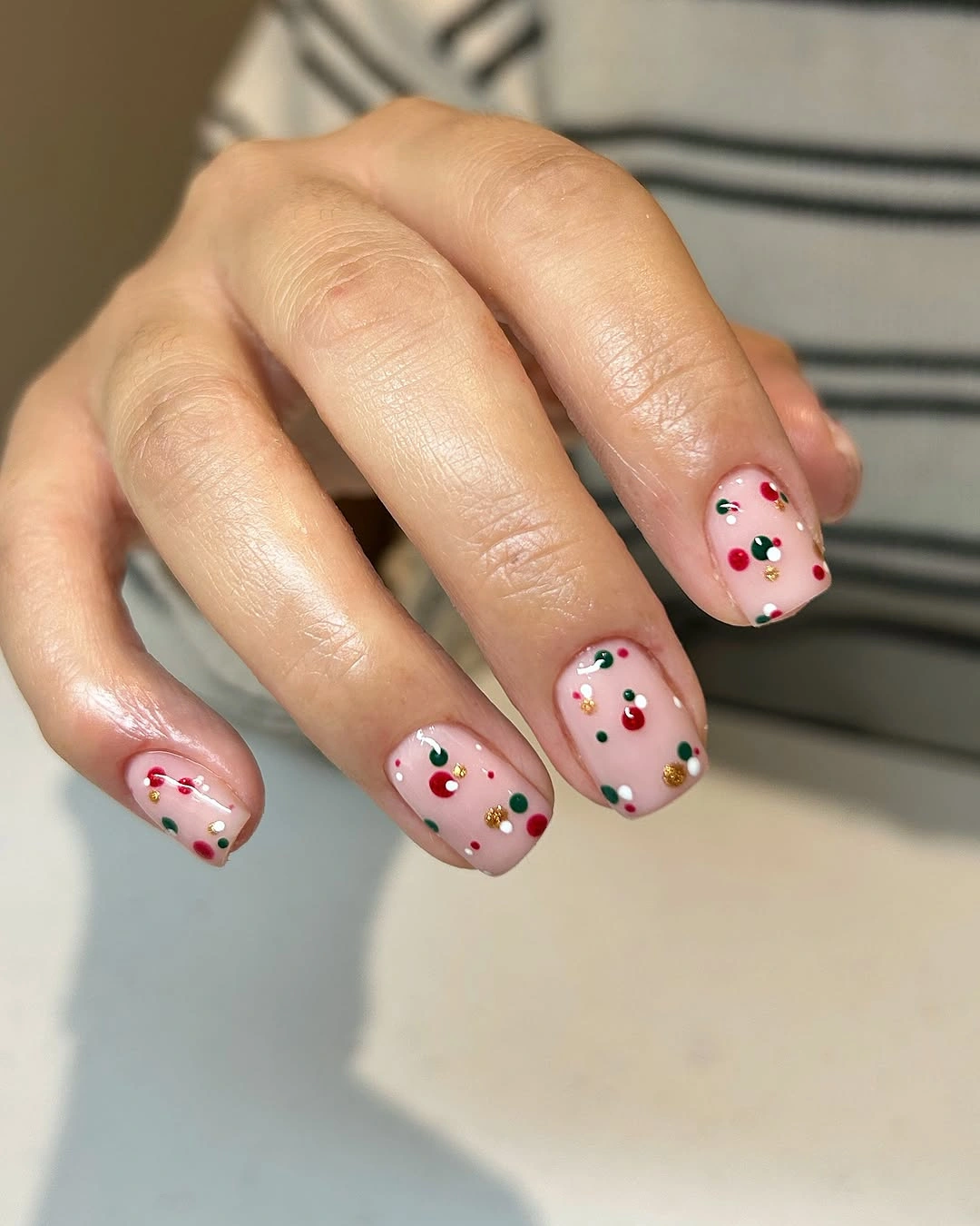 Short pale pink square nails scattered with red, green, and gold dots.