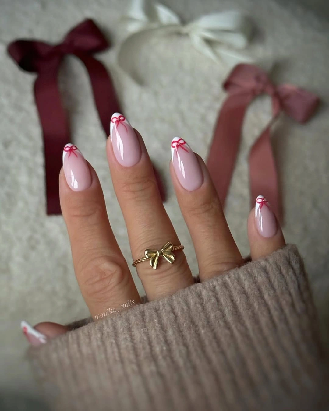 Pale pink almond nails with small red bows near their tips.