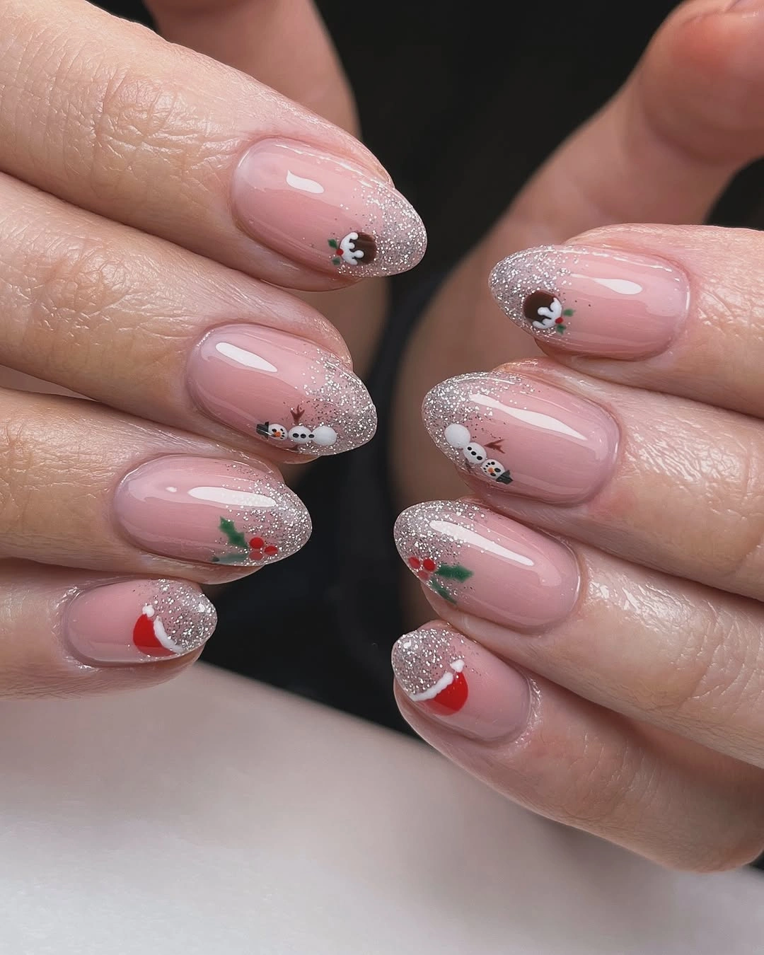 Glossy pink almond nails with silver glitter tips and miniature festive markings.