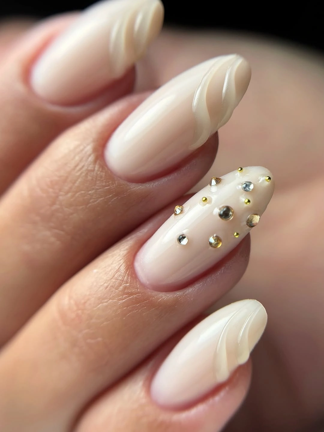Ivory almond nails with curved white ridges and scattered metallic dot accents.