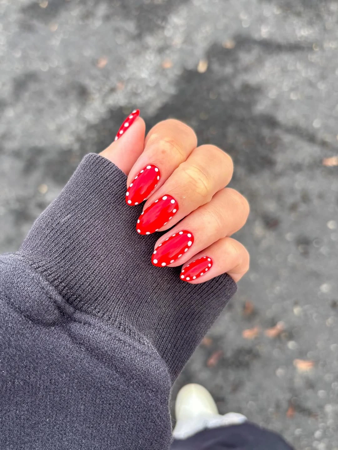 Bright red almond nails with small white dots tracing their edges.