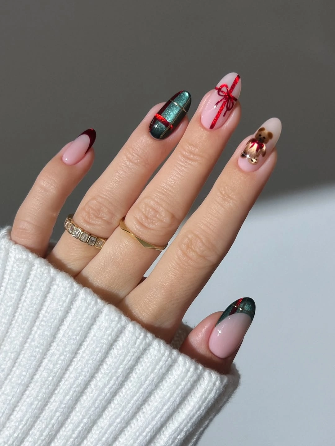 Pink almond nails with dark green tips, a red bow, and teal accents.