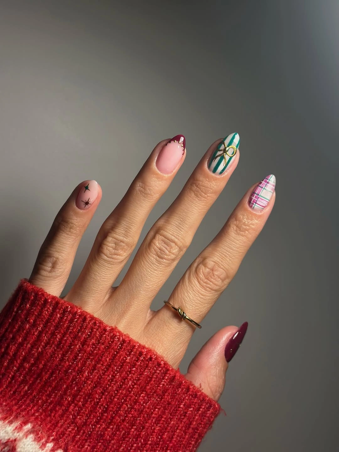 Nude almond nails with burgundy tips, green ribbons, and plaid accents.