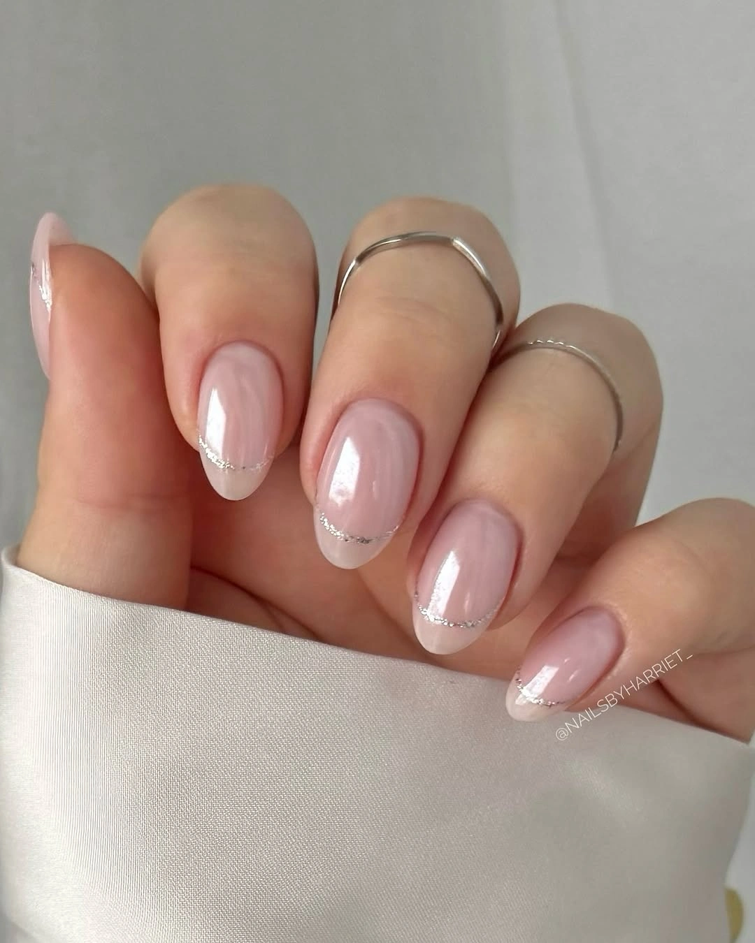 Short glossy pink nails with thin silver glitter French tips.